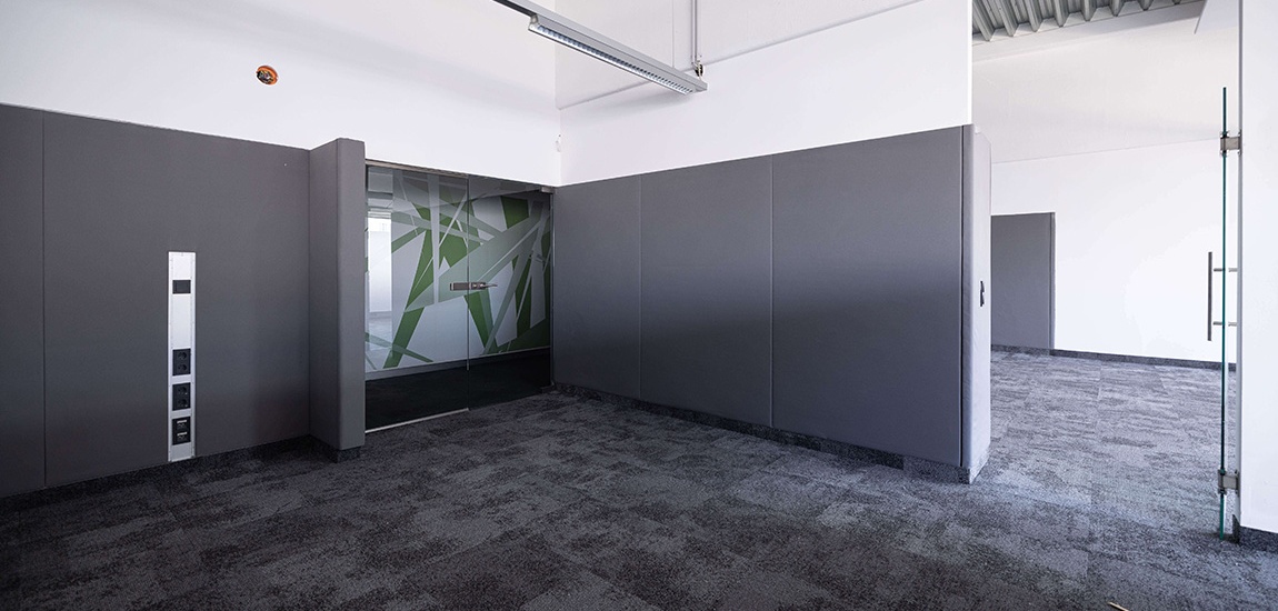 Ein leerstehender moderner Büroabteil mit schwarzen Pinwänden silbernen Steckdosen links und einem Glasverbau in der Mitte.